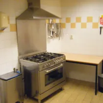 Een compacte keuken met een professioneel fornuis en afzuigkap, ideaal voor het bereiden van maaltijden of kleinere kookactiviteiten in een functionele omgeving.