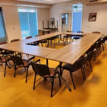 Een lichte en ruime vergaderzaal met tafels in U-opstelling, geschikt voor groepsbijeenkomsten en interactieve sessies.