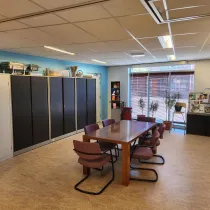 Een praktische ruimte met een grote houten tafel en comfortabele stoelen, ideaal voor vergaderingen of creatieve workshops. Grote ramen zorgen voor veel daglicht en een uitnodigende sfeer.