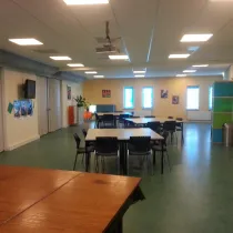 De grote zaal in het Buitenhuis is een veelzijdige ruimte die ideaal is voor grotere bijeenkomsten, evenementen of groepsactiviteiten. De zaal heeft een flexibele opstelling met tafels en stoelen die gemakkelijk aanpasbaar zijn aan verschillende behoeften. Het interieur is licht en ruim, met voldoende ramen die natuurlijk licht binnenlaten. Daarnaast zijn er moderne voorzieningen, zoals een projector en een televisie, waardoor deze ruimte uitstekend geschikt is voor presentaties en workshops.