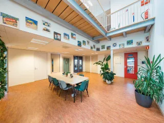 De ruime hal met groene wand, lichte kleuren en gezellige decoratie. Geschikt voor een gezellige kop koffie, om even te werken of een praatje te maken