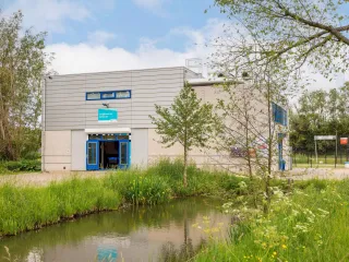 Een vierkant gebouw met witte bakstenen en blauwe kozijnen gelegen in het groen
