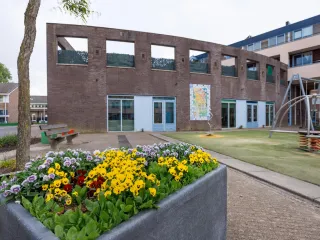 De Wippolder in Delft is een eigentijds ogend, laagbouwpand met een robuuste bakstenen gevel, waarbij de entree subtiel is benadrukt met een overstekend dakje en grote glaspuien die uitnodigend uitzicht bieden op de omliggende groenrijke pleinruimte.
