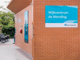 Het gebouw heeft een robuuste, hoekige uitstraling met warme bakstenen gevel en horizontale lijnen, ontworpen met een verfijnd contrast tussen stenen buitengevels en subtiel naar voren stekende houten volumes. Met een luifel boven de ingang en grote glaspartijen oogt het gebouw uitnodigend en afgestemd op het omliggende groene plein. 