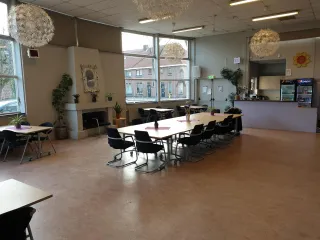 Deze lichte en flexibele ruimte is ideaal voor bijeenkomsten, workshops of maaltijden. Grote ramen zorgen voor veel daglicht, terwijl decoratieve planten en moderne lampen een warme sfeer creëren.