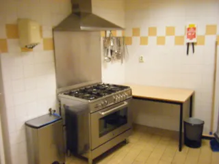 Een compacte keuken met een professioneel fornuis en afzuigkap, ideaal voor het bereiden van maaltijden of kleinere kookactiviteiten in een functionele omgeving.