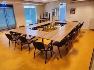 Een lichte en ruime vergaderzaal met tafels in U-opstelling, geschikt voor groepsbijeenkomsten en interactieve sessies.